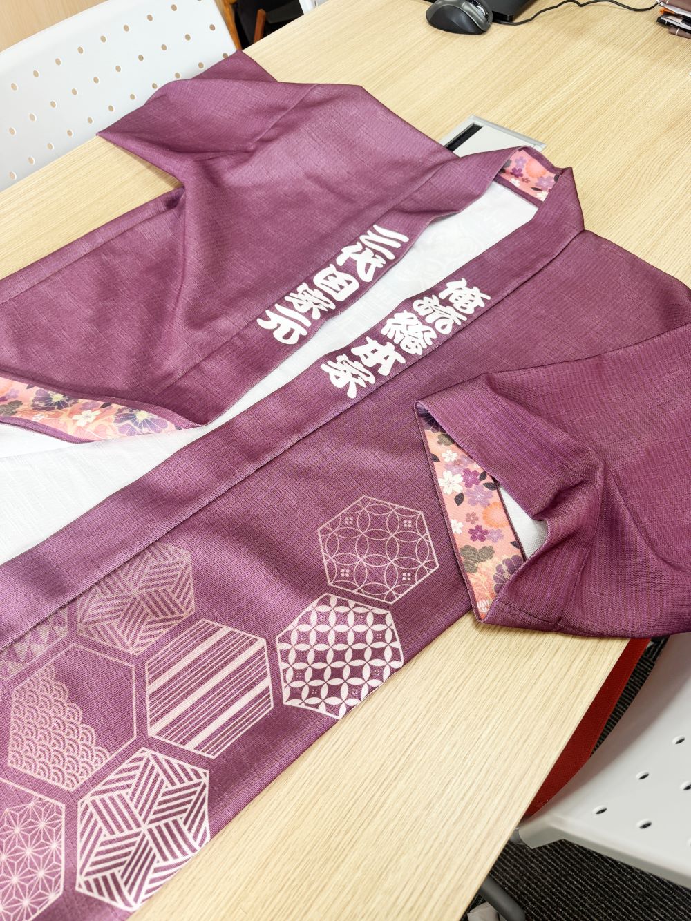 机の上に広げられた、紫色の伝統柄と白い文字が施された和風の法被（はっぴ）。